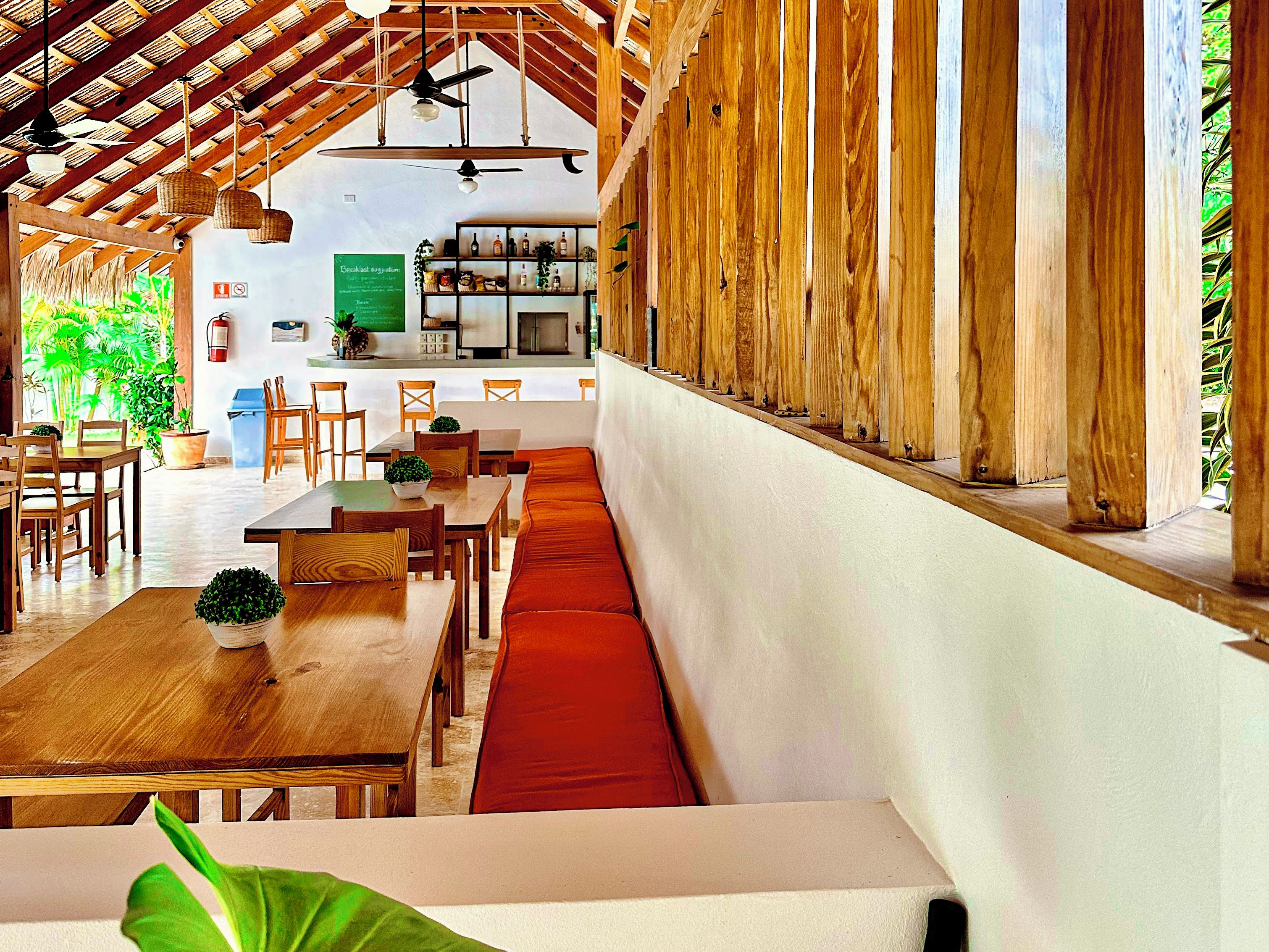 Un restaurant avec des meubles en bois, un long comptoir et un espace salon doté de coussins rouges.