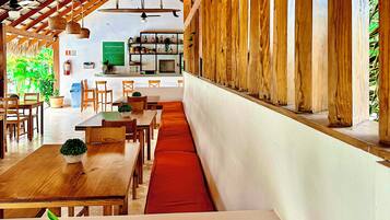 Un restaurant avec des meubles en bois, un long comptoir et un espace salon doté de coussins rouges.