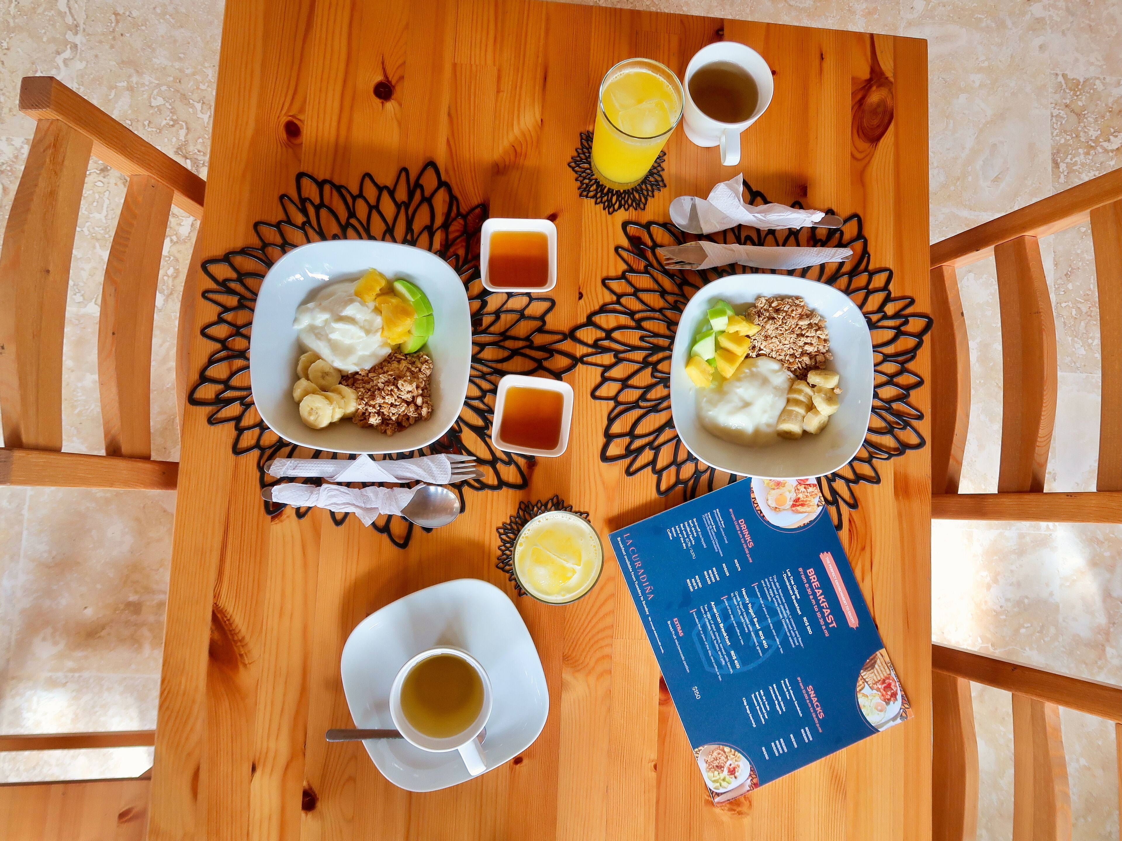 A breakfast setting with two plates of food, a menu, and a cup of tea on a wooden table.