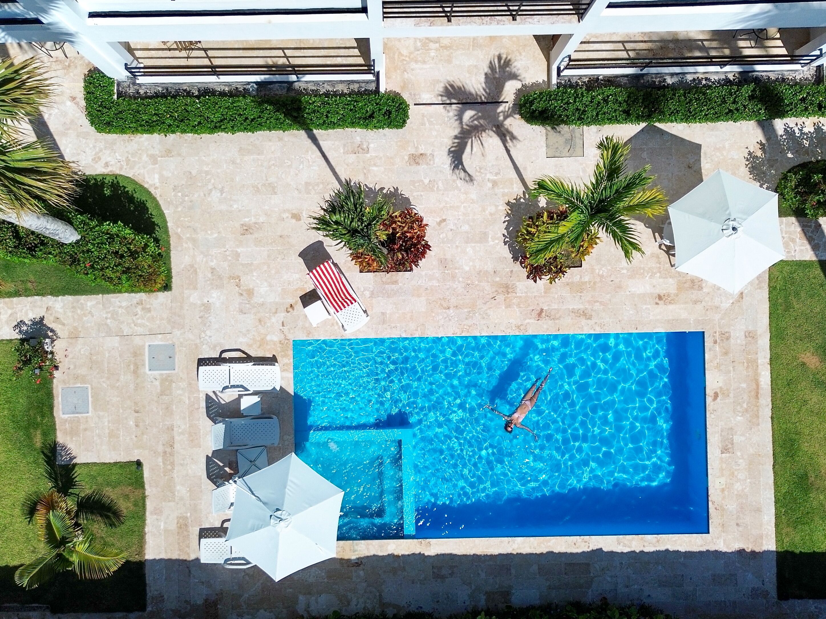 An aerial view of a swimming pool area with lounge chairs, umbrellas, and potted plants.