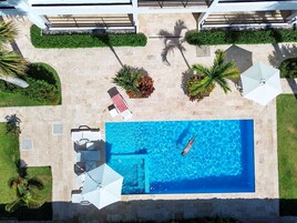 Vista aérea de un área de piscina con sillones de descanso, sombrillas y plantas en macetas.