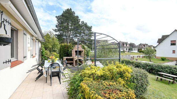 Et boligområde med terrasse, udendørs møbler, en murstensovn og en metalkonstruktion.