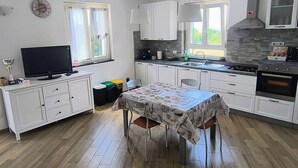 Een moderne keuken met witte kasten, een eettafel met stoelen, een televisie en een fornuis.