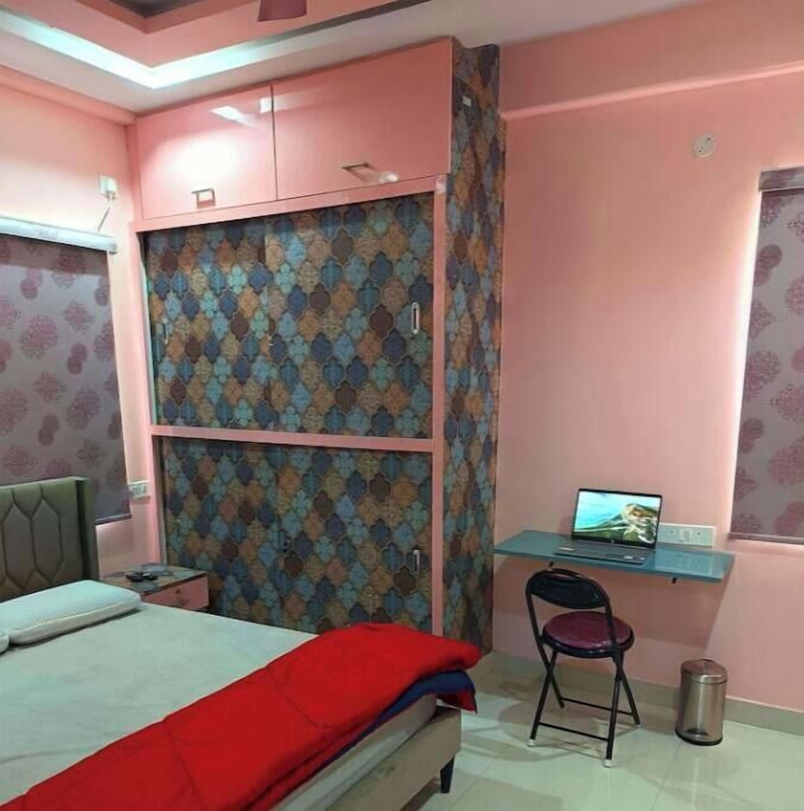 A bedroom with a bed, a desk with a laptop, a chair, and a wardrobe.