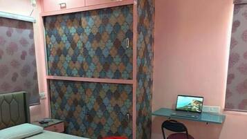 A bedroom with a bed, a desk with a laptop, a chair, and a wardrobe.