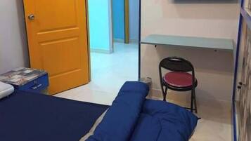Een kleine kamer met een bed, een stoel, een televisie aan de muur en een deur naar een andere kamer.