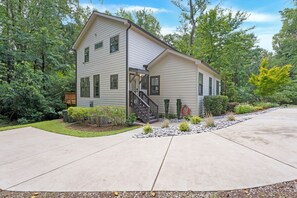 A two-story house with a front porch, a staircase leading to the entrance, and a well-maintained garden with various plants and a gravel pathway.
