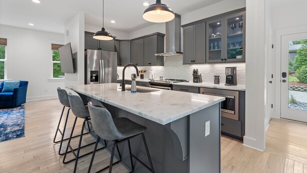 A modern kitchen with a central island, bar stools, and pendant lighting.
