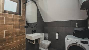 Une petite salle de bain avec un mur en bois, un lavabo blanc, des toilettes et un lave-linge.