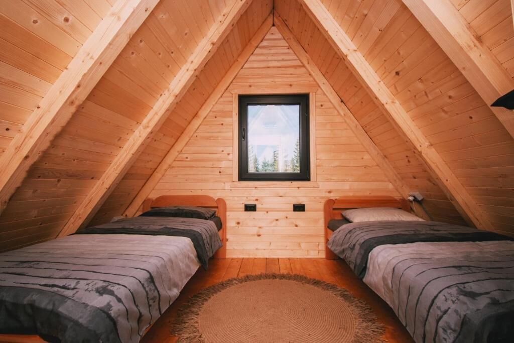 Quarto de sótão acolhedor com duas camas, uma janela pequena e paredes de madeira.