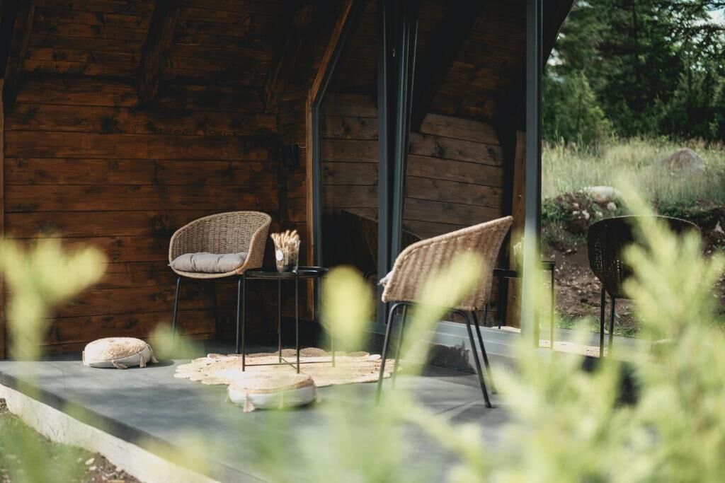 Une cabane en bois avec deux fauteuils en osier et une petite table, un sol en béton et une vue sur la verdure environnante.