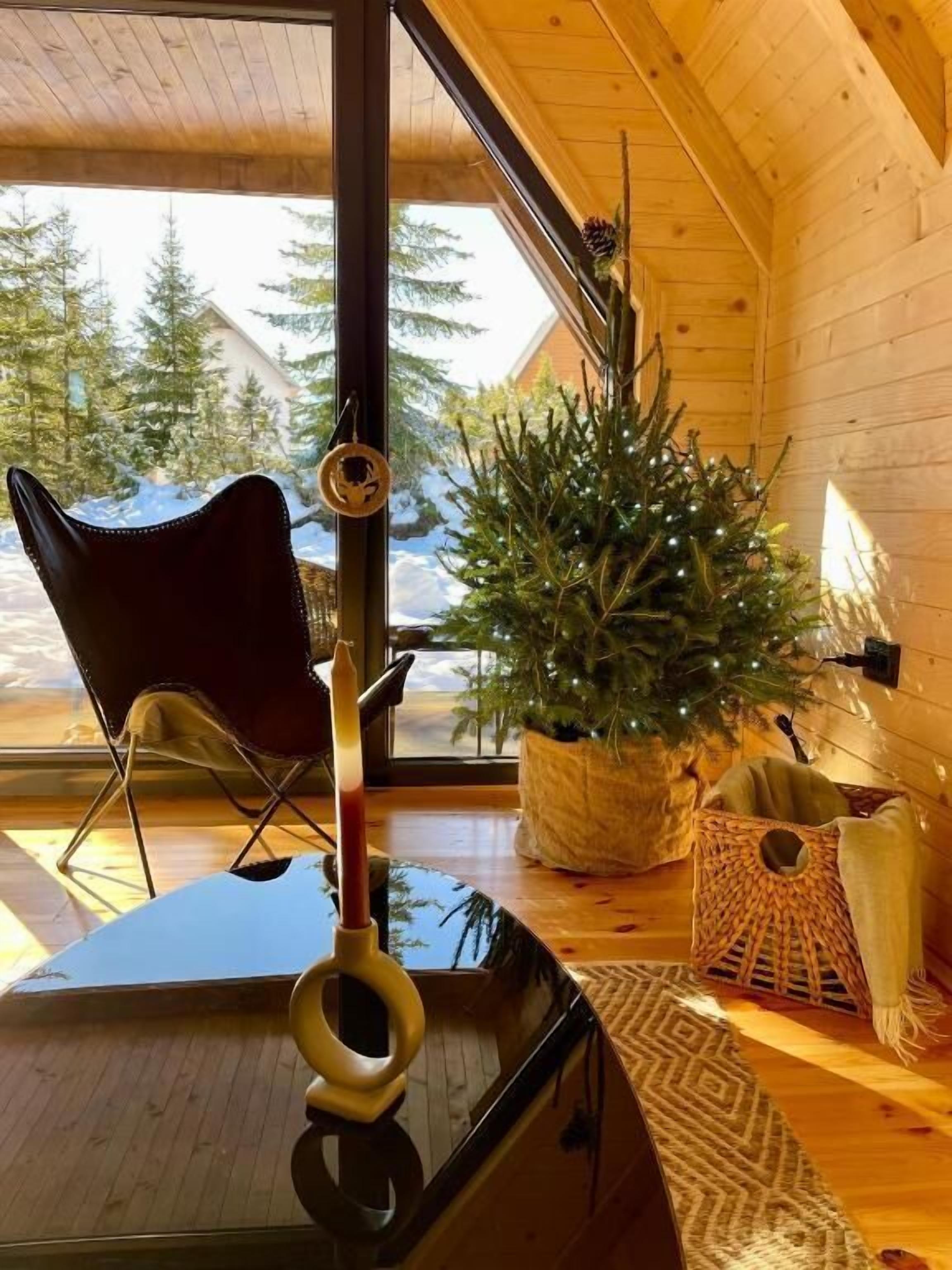 Ein gemütliches Blockhaus-Interieur mit Holzbalkendecke, einem Weihnachtsbaum, einem Sessel und einem kleinen Tisch.