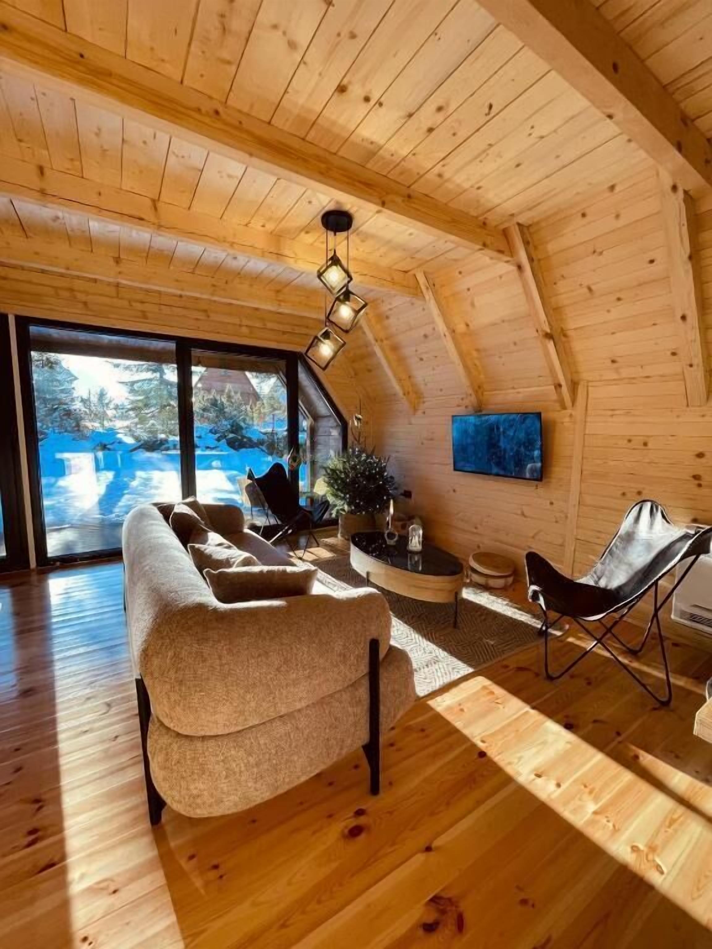 A cozy wooden interior with a sofa, a chair, and a TV on the wall.