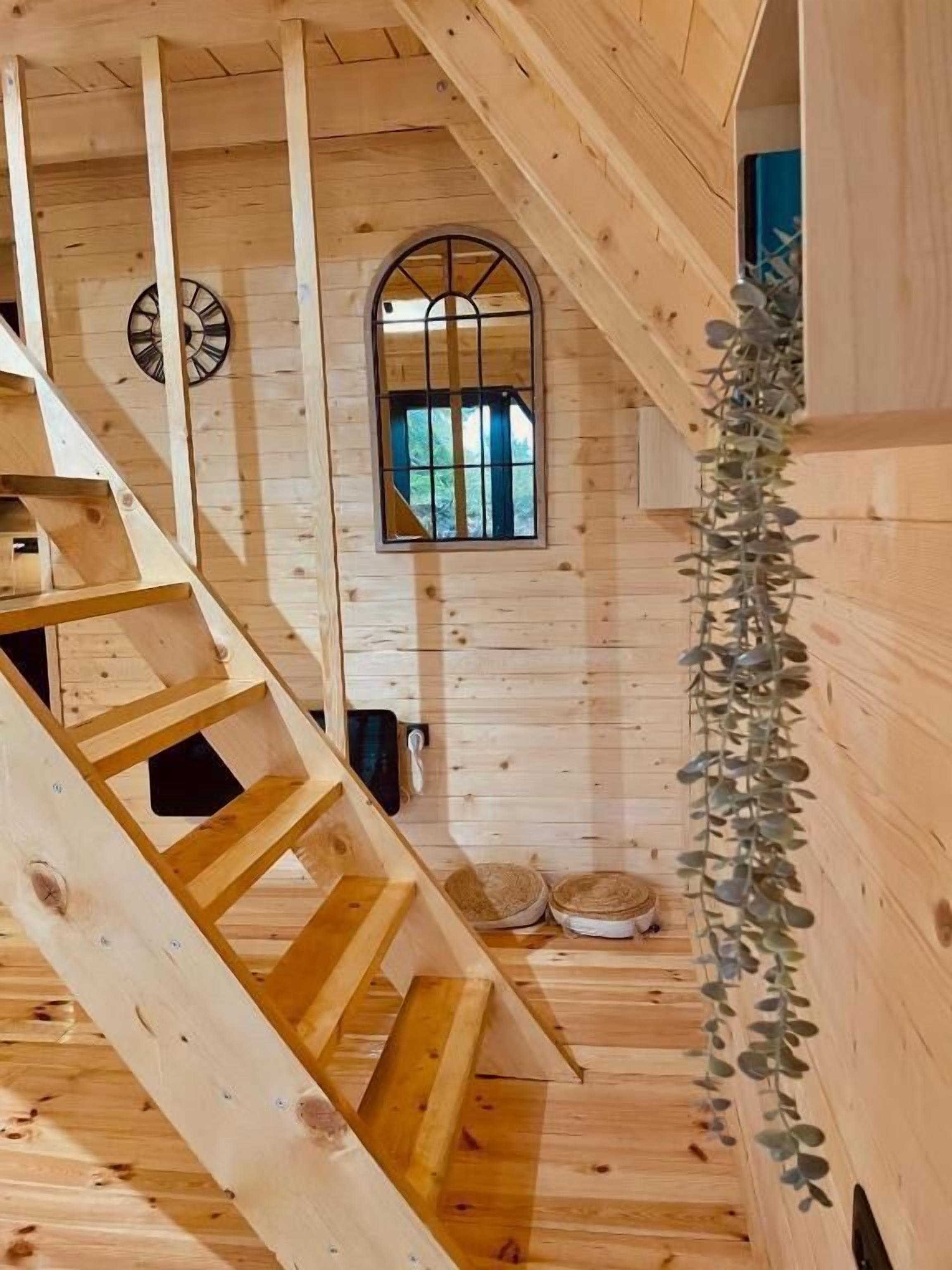 A wooden interior with a staircase, a window with bars, and a plant.