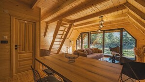 Un intérieur en bois comprenant un coin repas, un canapé et une vue dégagée grâce à de grandes fenêtres.