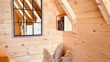 Interior de madeira com teto inclinado, janela com design em grade e cesta de palha com plantas secas.