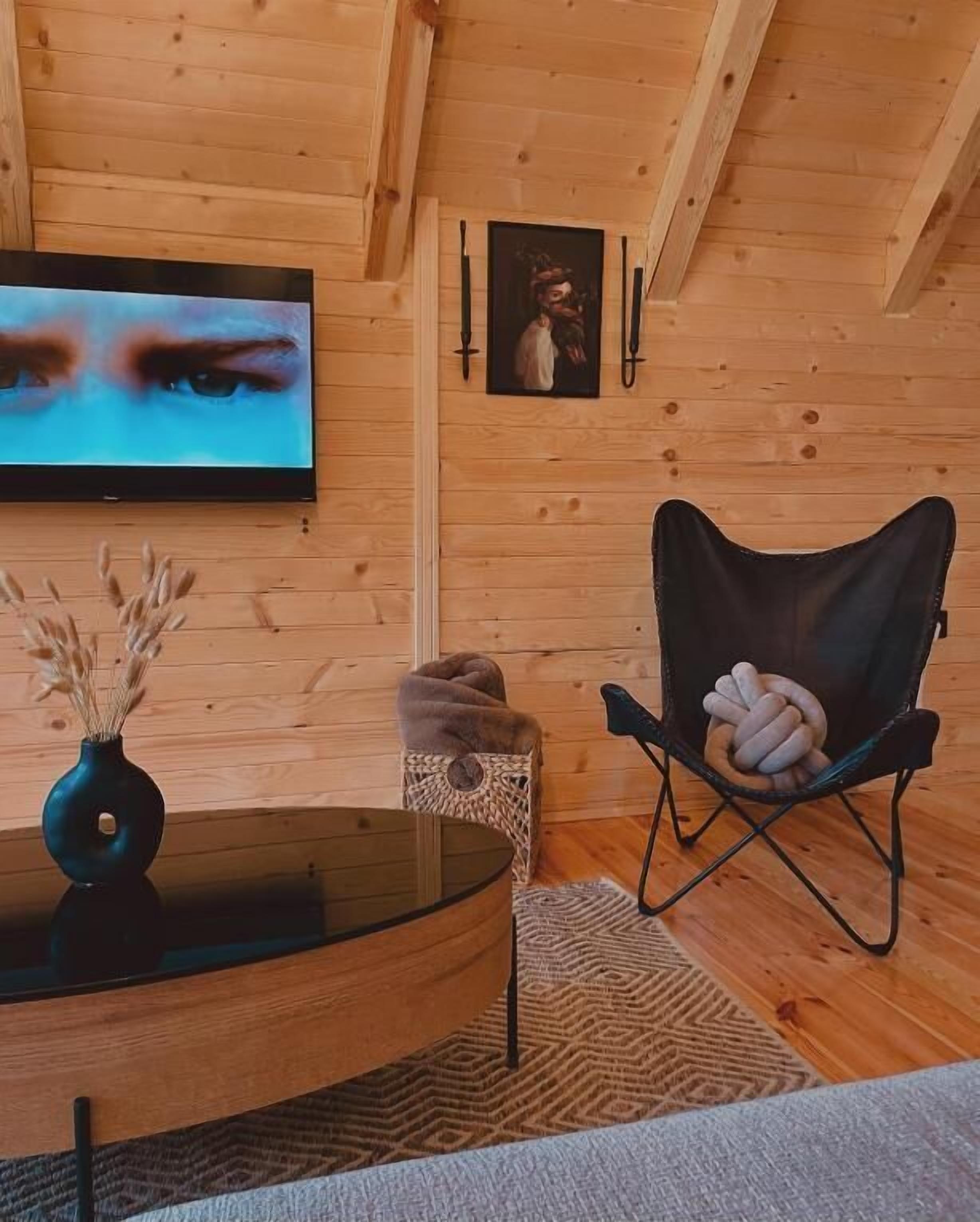 L’intérieur d’un chalet en bois chaleureux et accueillant, avec une télévision, un panier tressé et un fauteuil orné d’un motif noué.