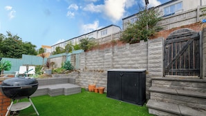 A backyard with artificial grass, a barbecue grill, a shed, and a stone wall.