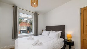 A neatly made bed with white linens and towels, a bedside lamp, and a window with curtains.