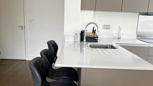 Eine moderne Küche mit weißer Arbeitsplatte, einer Edelstahl-Spüle und schwarzen Polsterstühlen.