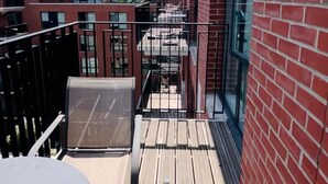 Ein Balkon mit Holzboden, Metallgeländer und Blick auf ein rot backsteins Gebäude.