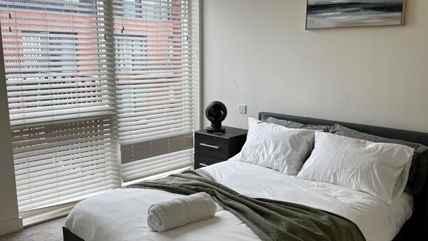 Ein Schlafzimmer mit einem Bett, weißer Bettwäsche, einer grünen Tagesdecke, einem Nachttisch mit Globus und einem Bild an der Wand.