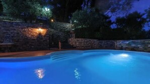 A swimming pool at dusk with stone walls and a stone staircase leading up to a lighted area.