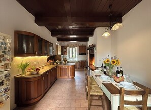 A kitchen with wooden cabinets, a central island, and a dining area with a table set for two. - Villa Cesari Tiberi - private pool and frescoes (Marsciano)