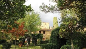 A stone building with a garden in front, surrounded by trees and shrubs.