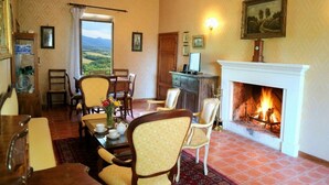 A room with a fireplace, dining table, chairs, and a view through a window.
