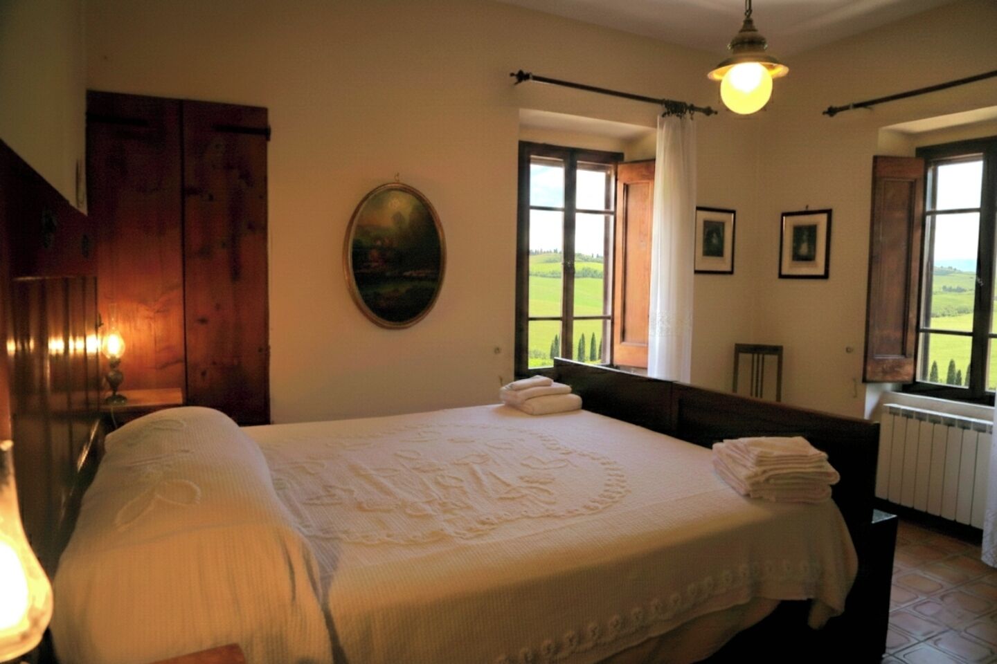 A bedroom with a large bed, a wooden wardrobe, a painting, and a window with a view of the countryside.