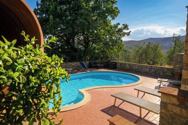 A curved outdoor swimming pool with lounge chairs and a stone wall, surrounded by greenery and a mountainous backdrop. - Villa Cesari Tiberi - private pool and frescoes (Marsciano)
