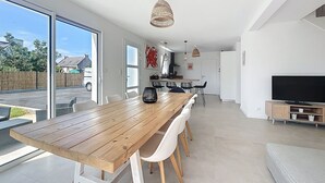 A modern kitchen with white cabinets, a wooden dining table, and a large TV. - House Roscoff 5 mn walk from the port (Roscoff)
