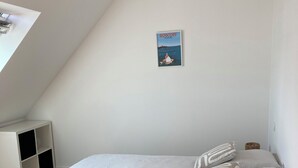 A bedroom with a bed, a small shelf unit, a picture on the wall, and a woven basket. - House Roscoff 5 mn walk from the port (Roscoff)