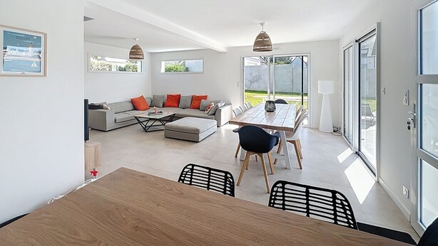 A modern living room with a sofa, coffee table, and dining table. There are large windows and a view of the outdoors. - House Roscoff 5 mn walk from the port (Roscoff)