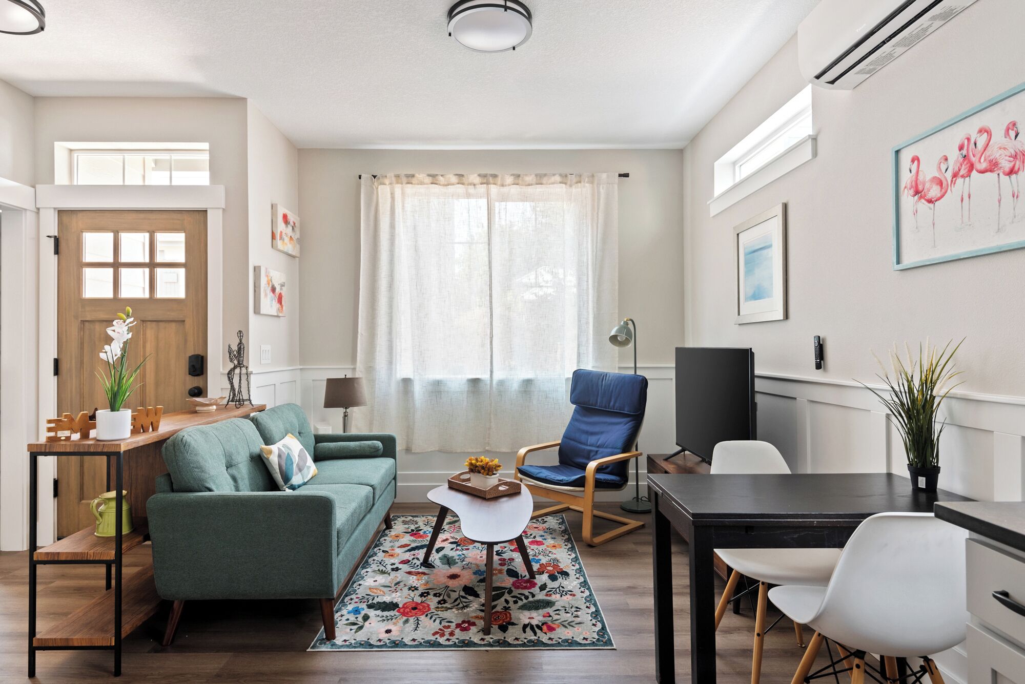 Ein modernes Wohnzimmer mit einem grünen Sofa, einem blauen Sessel, einem Esstisch mit Stühlen und einem großen Fenster mit durchsichtigen Vorhängen.