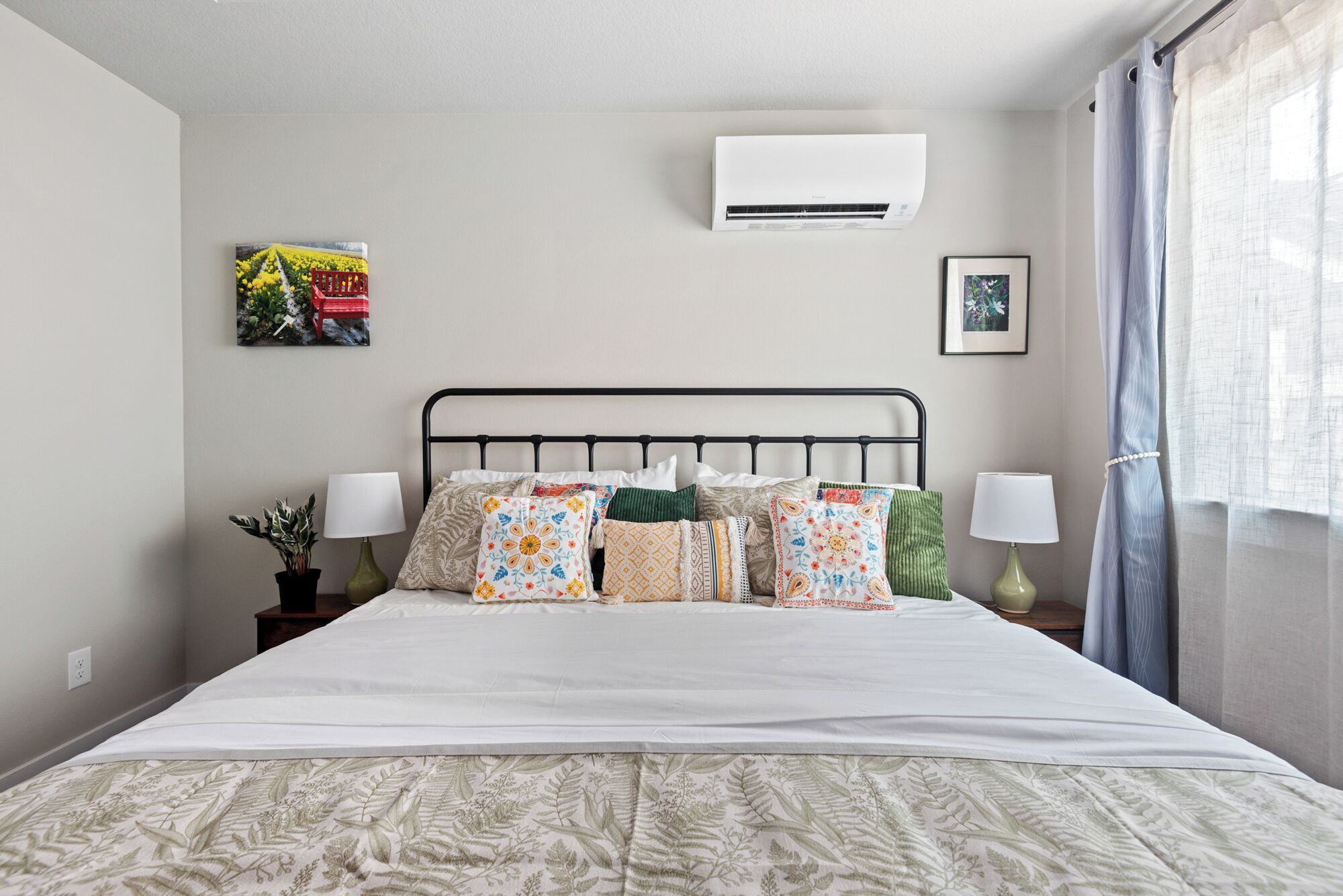 Een netjes ingerichte hotelkamer met een bed, twee nachtkastjes, een wandairconditioner en een raam met gordijnen.