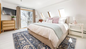 A bedroom with a large bed, a dresser, a TV, and a window with curtains.