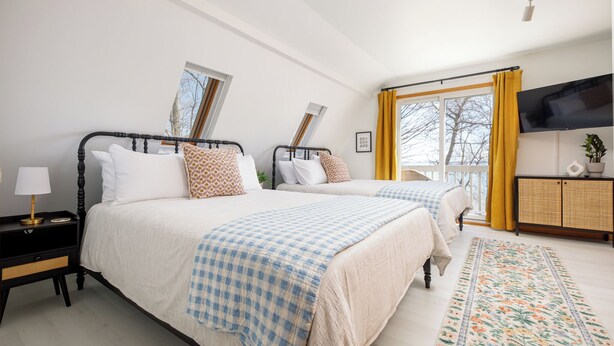 A bedroom with two beds, a television, and a window with curtains.