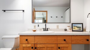 A bathroom with a white toilet, wooden vanity with a sink, and a large mirror.