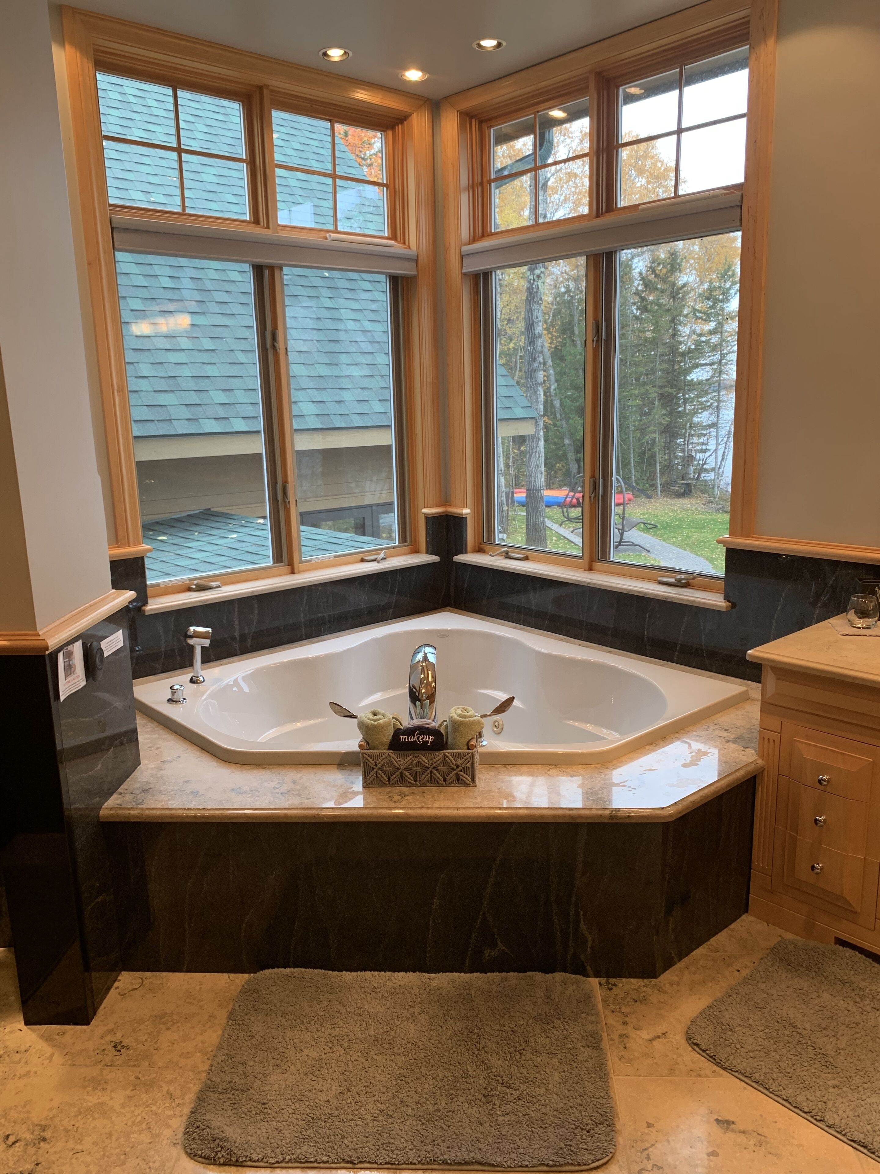 A bathroom with a large freestanding bathtub, a vanity with a mirror, and a window with a view of trees and a lake.