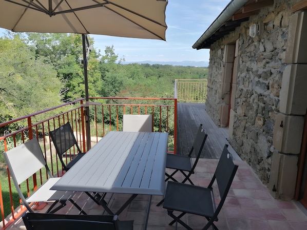Une terrasse extérieure avec une table et des chaises, une rambarde rouge et un mur en pierre.