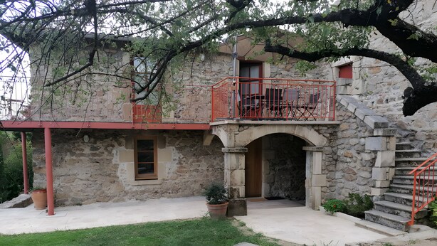 A stone building with a balcony, a staircase, and a small garden area.