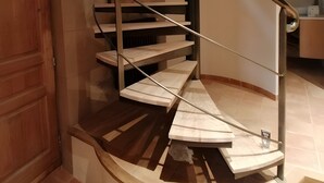 A spiral staircase with a wooden finish and metal handrails, leading to an upper floor.