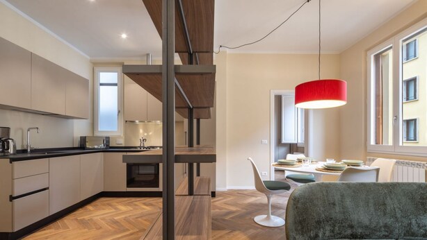 Eine moderne Küche mit Holzboden, einem Essbereich mit roter Pendelleuchte und Blick ins Freie durch ein Fenster.