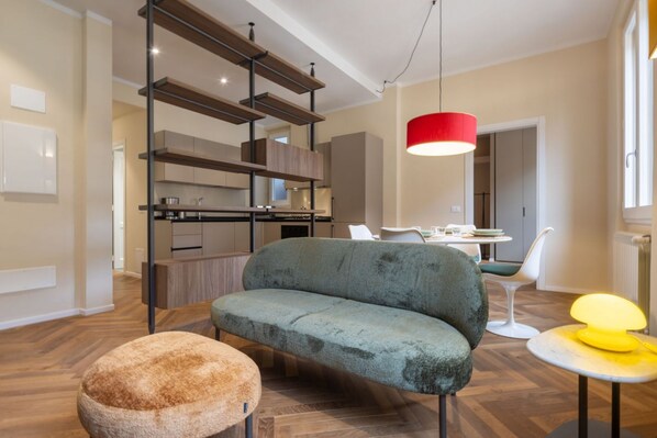 A modern kitchen with wooden shelves, a dining area with a white table and chairs, and a sofa.