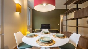 Uma área de refeições com uma mesa redonda, cadeiras brancas e uma luminária pendente vermelha.
