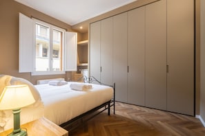 A bedroom with a bed, a nightstand with a lamp, a wardrobe, and a window with curtains.