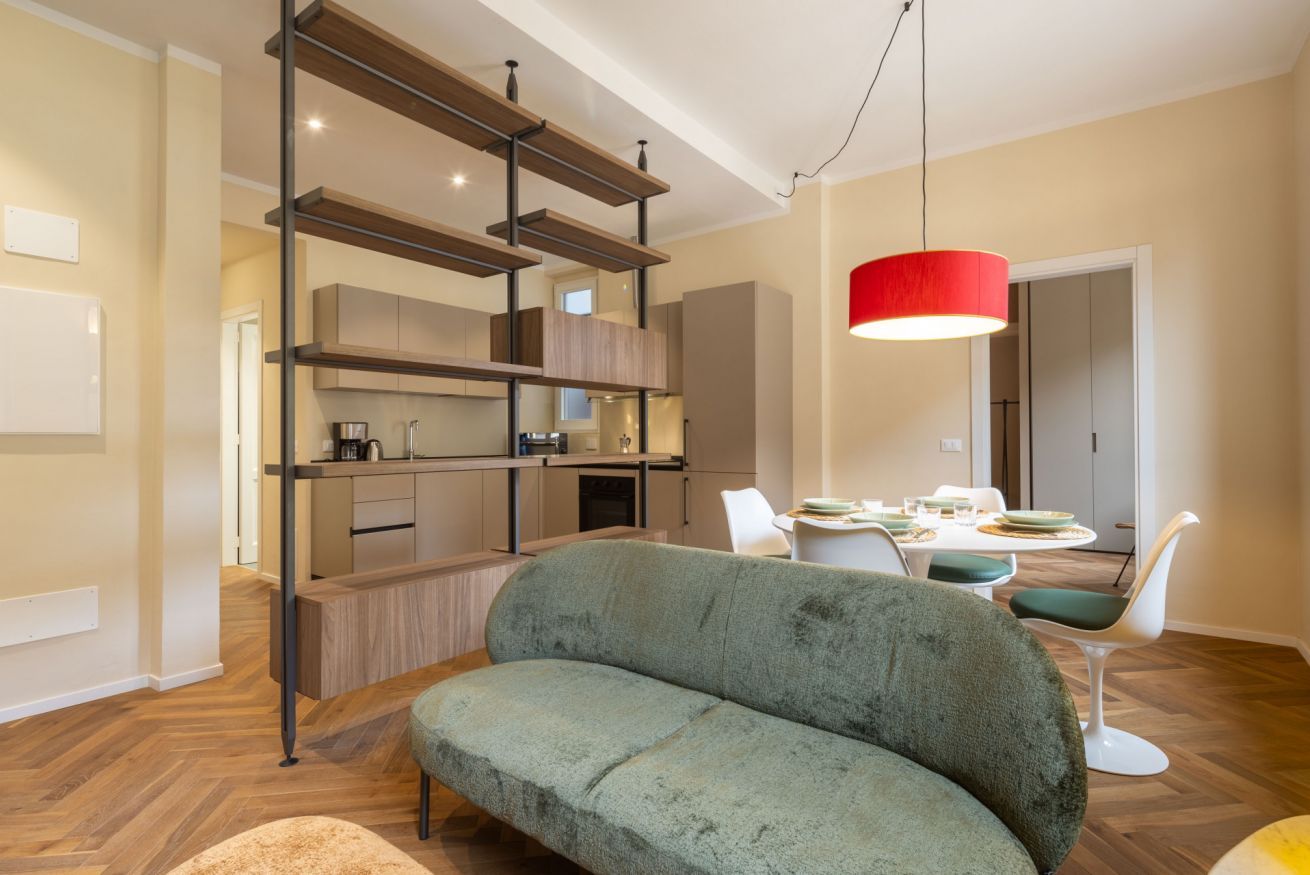 A modern living room with a sofa, dining table, and a kitchen area with wooden shelves.