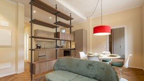 Uma sala de estar moderna com sofá, mesa de jantar e área de cozinha com prateleiras de madeira.